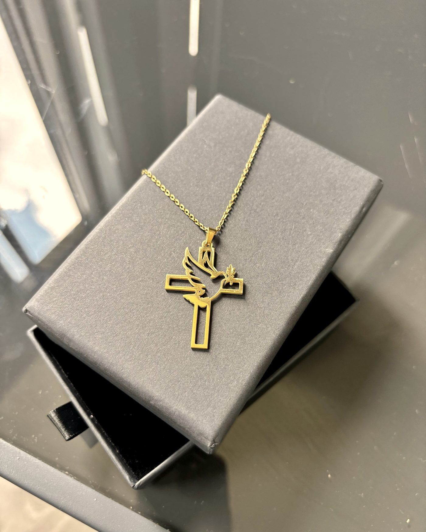 A gold dove-and-cross pendant resting on a grey gift box.